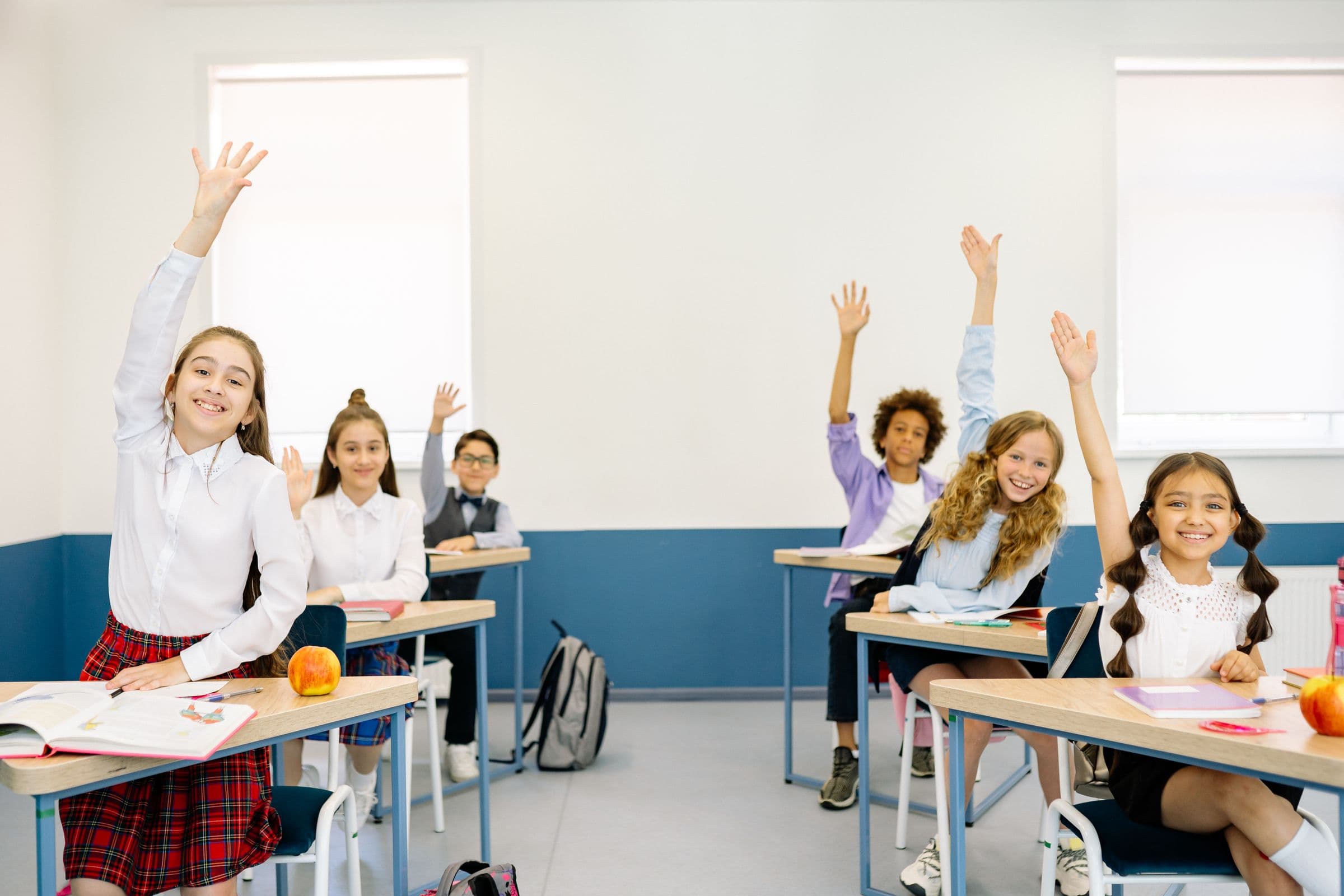 A bright classroom of diverse students raising their hands