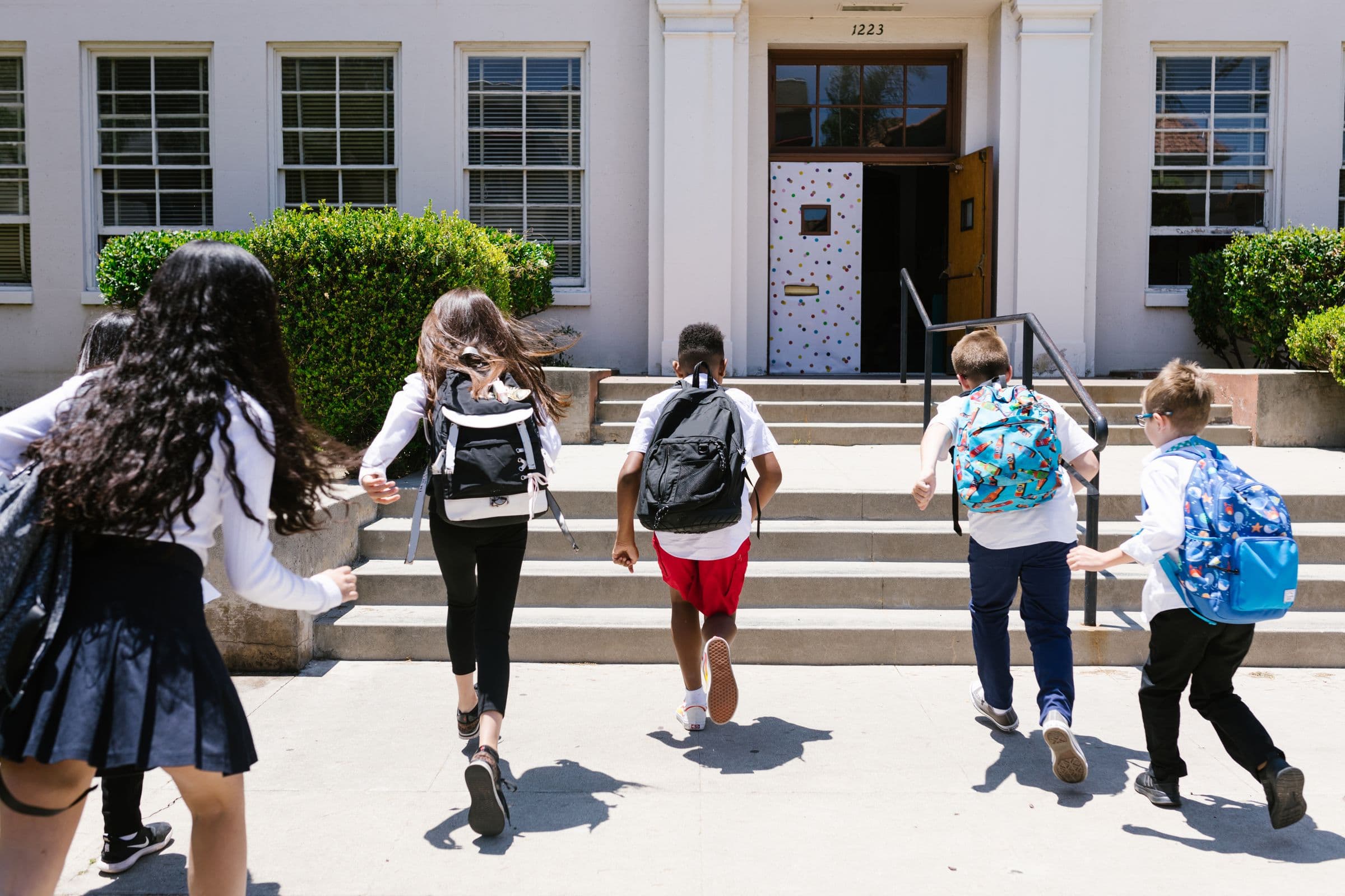 Diverse students wearing backpacks heading up the steps into school