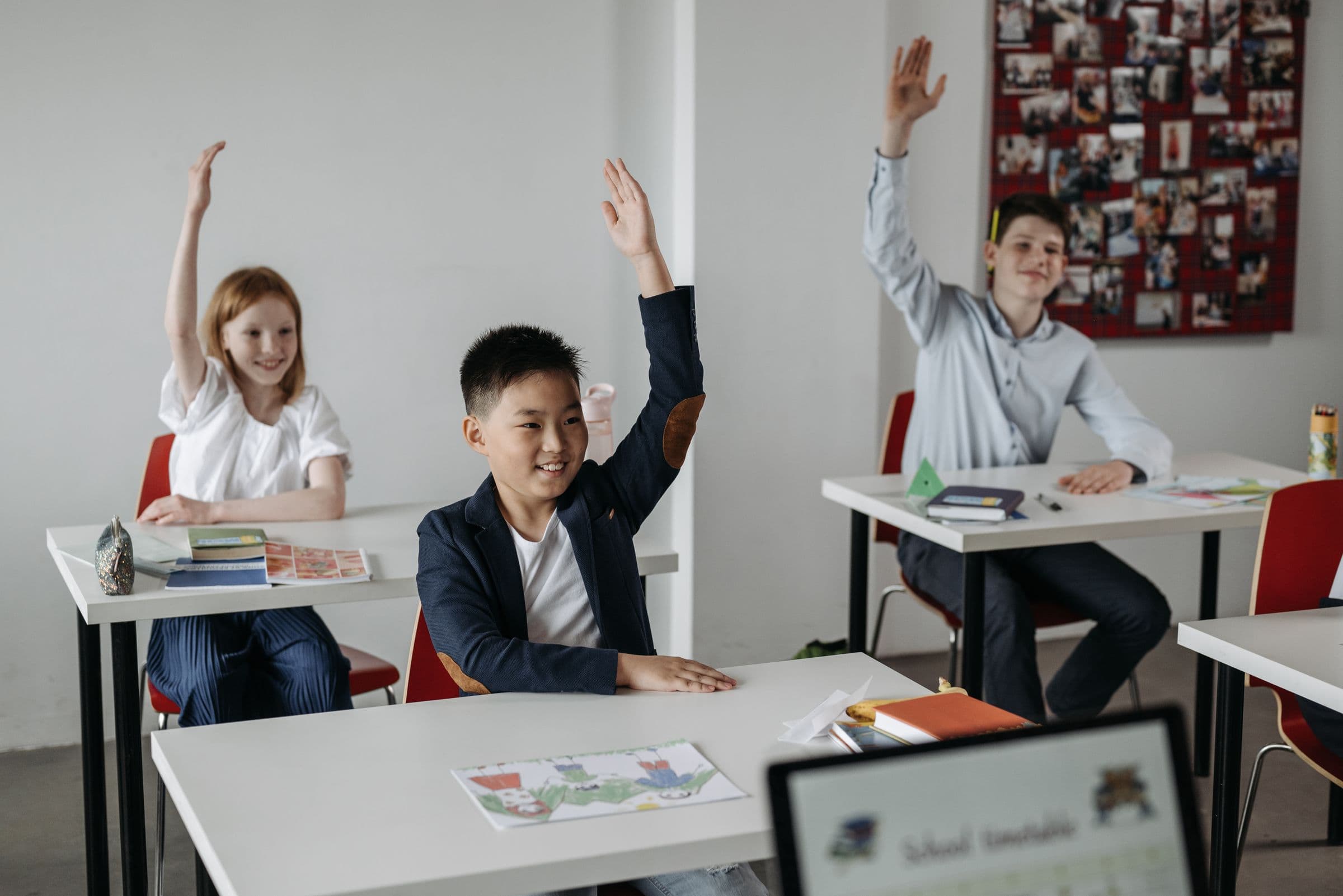 Diverse, engaged students raising their hands in a bright classroom
